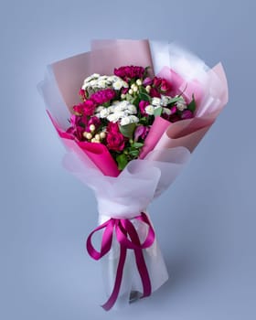 Bouquet of pink and white flowers wrapped in floral paper on a blue background. Original bouquet of pink roses, eustoma and white little asters. Concept of Women's Day, Mother's Day and Birthday.