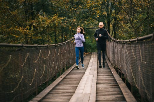 Family spends time with benefit. Loving young sports couple runners running on an old suspension bridge on a cool autumn day. Fitness, sport, people, exercising and lifestyle concept