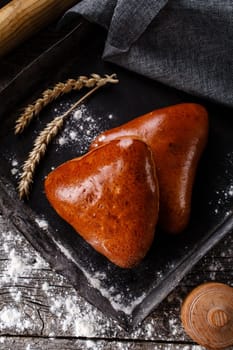Close up of two fresh baked buns on dark baking plate. Top view of buns lying near burlap and ears of wheat on wooden table sprinkled with flour. Baking concept with rye and flour.
