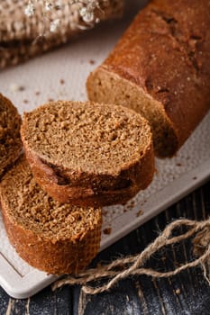 Homemade bread. Slices of freshly baked traditional brown bread with crispy crust. Close up of bread lying on white kitchen board on dark wooden table. Concept of baking bread products.