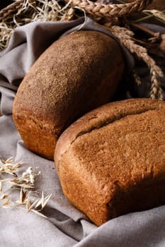 Rural bread. Country still life on which two loaves of fresh homemade rye bread lie on burlap cloth. Close up of uncut bread with brown crust lying on gray cloth near natural elements.