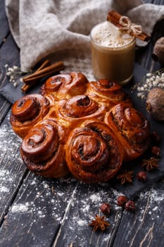 Freshly baked cinnamon buns with spices and stuffing with coffee drink on wooden table. Close up of buns on black methal board on table near Christmas spices. Christmas baking concept.