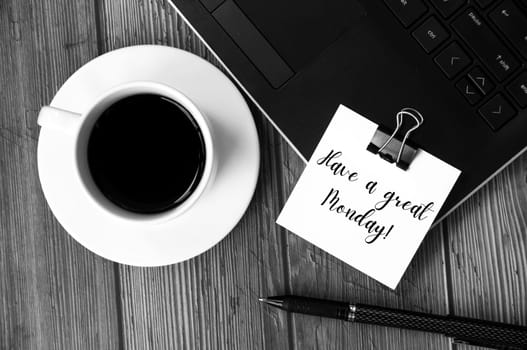 Have a great Monday text on white notepad with laptop, coffee cup and pen in black and white background. Greetings concept.