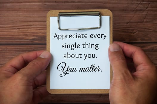 Hand holding paper holder board with text on white notepad - Appreciate every single thing about you. You matter. Inspirational and motivational quotes.