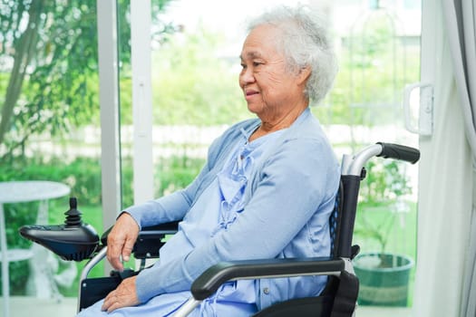 Asian elderly woman disability patient sitting on electric wheelchair in park, medical concept.