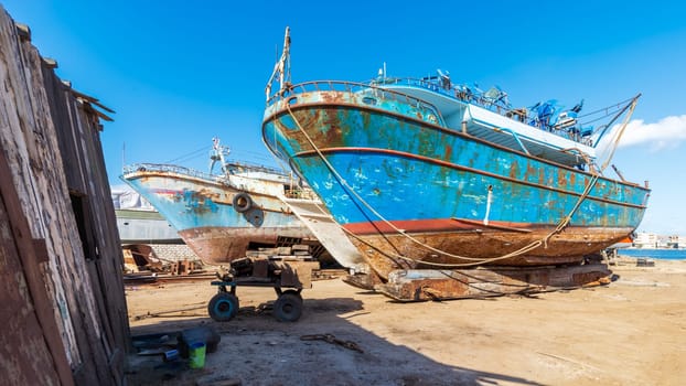Old rusty vessels under repairing located on grungy dry dock in shipyard against blue sky on sunny day in old shipbuilding plant