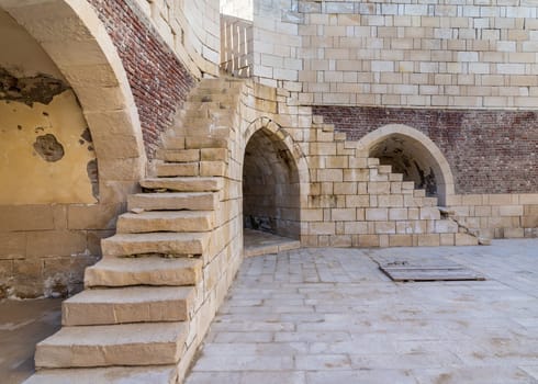 Exterior shot of ancient brick building with two perpendicular shabby stone stairways and two crumbling arched alcoves on street
