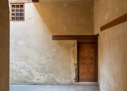 Wooden aged decorated door and small window covered with wooden grid on grunge stone wall