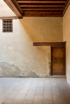 Wooden aged decorated door and small window covered with wooden grid on grunge stone wall and wood timber ceiling