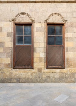 Facade of old abandoned stone decorated bricks wall with two adjacent arched wooden shutter windows