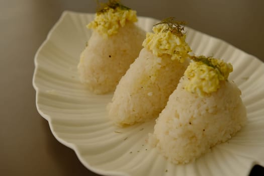 Plate with traditional Japanese onigiri with egg on brown background and beautiful white plate with leaf shape.