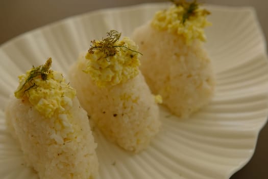 Plate with traditional Japanese onigiri with egg on brown background and beautiful white plate with leaf shape.