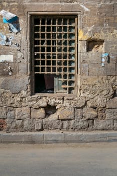 Old abandoned stone bricks wall with one closed grunge broken wooden window covered by wooden grid, Dard El Ahmar district, Cairo, Egypt