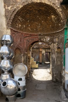 Arched passage between shabby houses with Egyptian traditional aluminum utensils stacked by wall in old Cairo city, Egypt on daytime