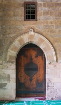 Vaulted closed decorated wooden grunge door in bricks stone wall at public historic Al Moaayad Mosque, Cairo, Egypt