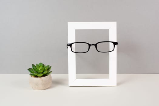 Home interior poster mock up with wooden frame, eyeglasses and cactus in a pot, gray wall background, copy space for text and pictures