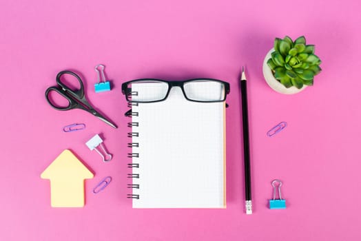 Empty notebook with a pen, eyeglasses and a cactus on a pink colored desk, brainstorming for new ideas, writing a message, home office workplace