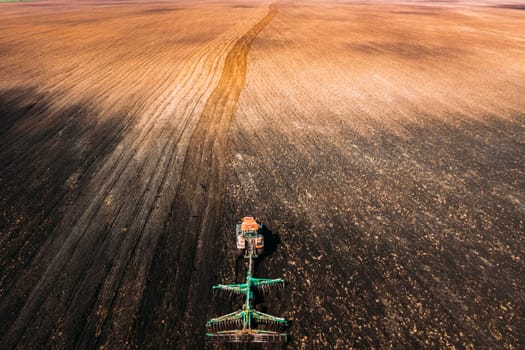 Aerial View. Tractor Plowing Field In Spring Season. Beginning Of Agricultural Spring Season. Cultivator Pulled By A Tractor In Countryside Rural Field Landscape.