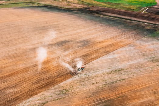 Aerial View. Tractor Plowing Field In Spring Season. Beginning Of Agricultural Spring Season. Cultivator Pulled By A Tractor In Countryside Rural Field Landscape.