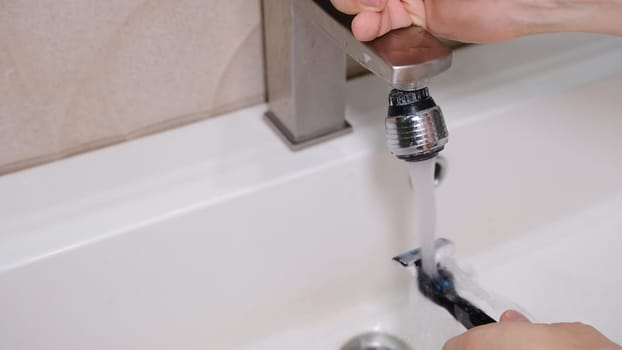 Cleaning shaving razor in bathroom sink. Rinsing off razor with water