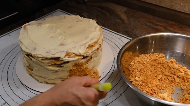 Cooking multi-layered cake Napoleon - baked cake layers, raw dough. Man covet cake sides by the crubms from the puffs.