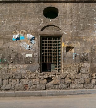 Old abandoned stone bricks wall with one closed grunge broken wooden window covered by wooden grid, Dard El Ahmar district, Cairo, Egypt