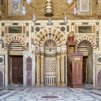 Colorful decorated marble wall with Mihrab - niche - and wooden minbar at public historic mosque of Sultan Barquq, El Moez Street, Old Cairo, Egypt