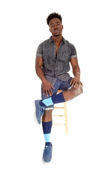 A handsome young African American man in shorts and sneakers sitting.on a chair looking serious, isolated for white background..