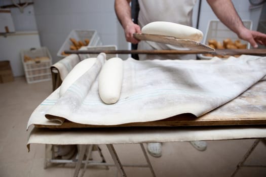Baker holding the oven slice with raw bread. Manufacturing process of spanish bread