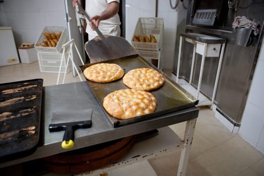 Elaboration process of traditional spanish olive oil pancakes. Baker taking fresh baked pancakes from oven