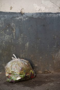 Plastic bag full of trash in front of dirty wall