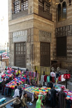 Cairo, Egypt- January 16 2016: Stalls with colorful clothes located outside old shabby Sultan al Ghuri Mausoleum building on Moez street