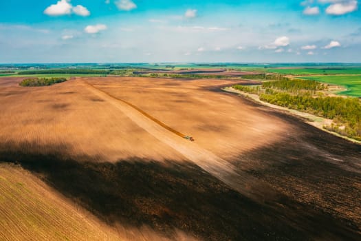 Aerial View. Tractor Plowing Field In Spring Season. Beginning Of Agricultural Spring Season. Cultivator Pulled By A Tractor In Countryside Rural Field Landscape.