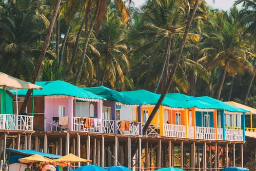 Canacona, Goa, India. Famous Painted Guest Houses On Palolem Beach Against Background Of Tall Palm Trees In Sunny Day.
