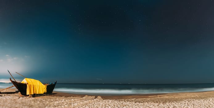 Goa, India. Real Night Sky Stars. Natural Starry Sky Blue Color Above Sea Seascape Ocean Beach. Background. Parked Old Wooden Boat At Coast. Panorama, Panoramic View.