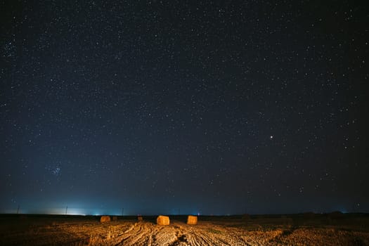 Night Starry Sky Above Haystacks In Summer Agricultural Field. Night Stars Above Rural Landscape With Hay Bales After Harvest. Agricultural Concept.