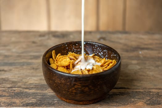 Cereal in wooden bowl with milk splash on blurred wooden