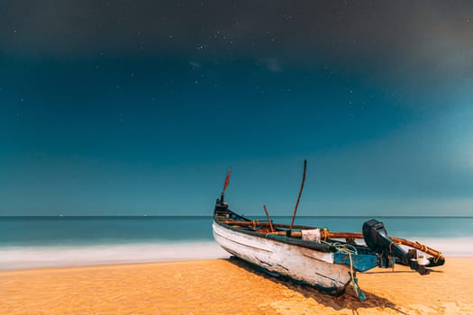 Goa, India. Real Night Sky Stars. Natural Starry Sky Blue Color Above Sea Seascape Ocean Beach. Background. Parked Old Wooden Boat At Coast.