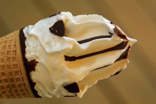 A close up of an ice cream cone with vanilla ice cream and chocolate icing.