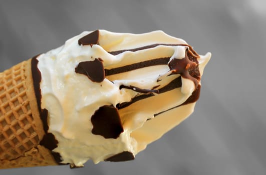 A close up of an ice cream cone with vanilla ice cream and chocolate icing.