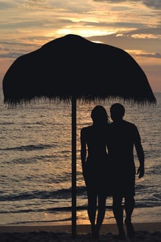 Romantic couple on the beach under straw umbrella hugging at sunrise