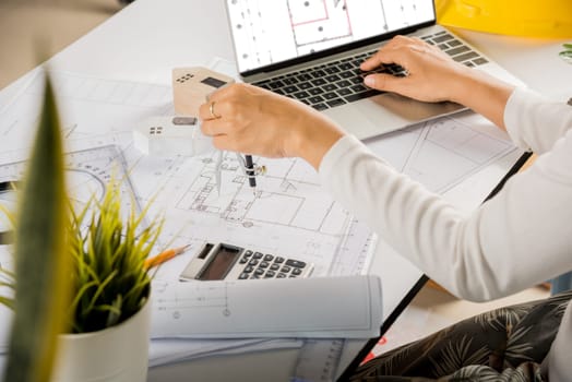 Architectural project workplace. Architect typing laptop keyboard to review design of house before editing or sketching with compass on plan blueprint paper on table desk at architecture office