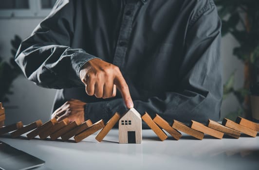 Business risk plan real estate protection. Man hand blocks wood block from many row falling wooden block like domino to house model, Insurance ideas to prevent loss concept