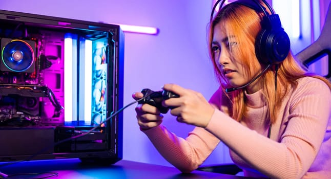 Gamer using joystick controller for virtual tournament plays online video game with computer neon lights, woman wear gaming headphones playing live stream esports games console at home, Esport concept