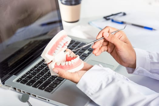 Oral dental hygiene. Dentist female holding professional stomatology tool and pointing healthy tooth model and explaining patient at clinic office and teeth X-ray on laptop screen, dental healthcare