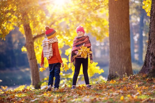 Children with colourful leaves in their hands in autumnal park. Consept of friendship and freedom.