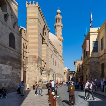 Cairo, Egypt- November 23 2019: Moez Street with local visitors, Minaret of Sultan Barquq Mosque, and Sabil-Kuttab of Katkhuda historic building at the far end, Gamalia district, Old Cairo