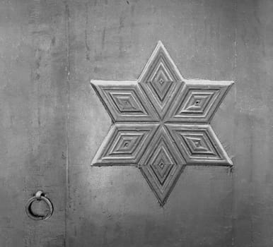 Black and white of decorations based on octagon star of David engraved on wooden grunge door with metallic door ring