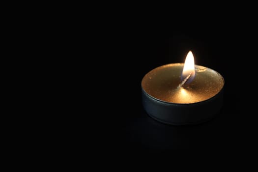 Burning candle close-up on a black background with copy space.