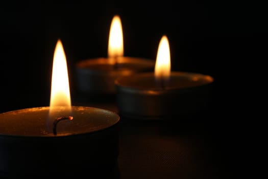 Three burning candles close-up on a black background with copy space. Blurred background.